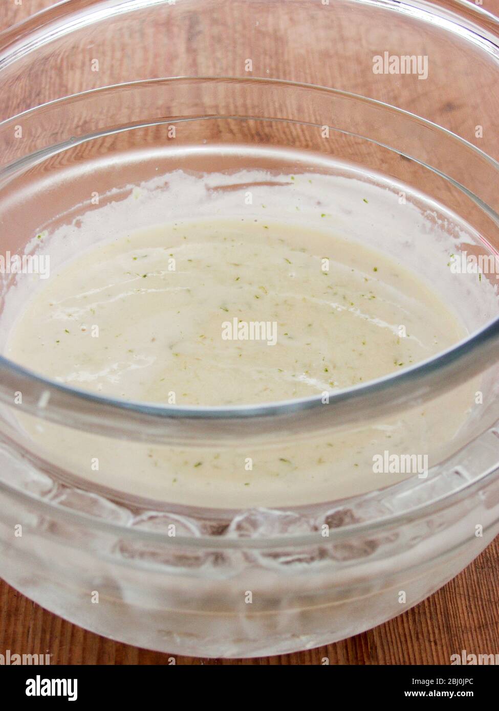 Thickened custard with gelatine and lime zest cooling in a bowl resting in a bigger bowl of ice water - Stock Photo