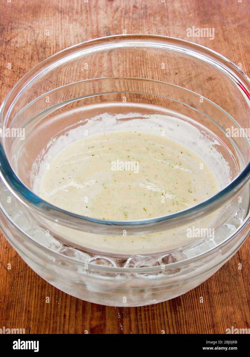 Thickened custard with gelatine and lime zest cooling in a bowl resting in a bigger bowl of ice water - Stock Photo