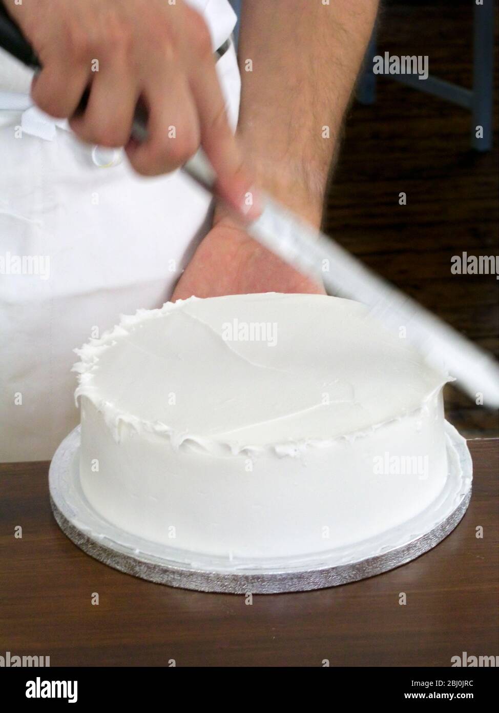 Giving iced cake a spiky edge with palette knife lifting points from soft icing - Stock Photo
