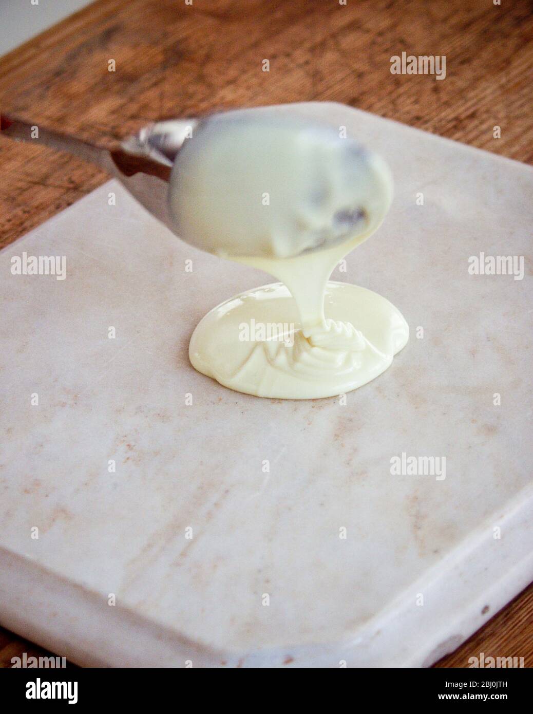 Spreading white chocolae onto marble slab to make choco;ate curls - Stock Photo