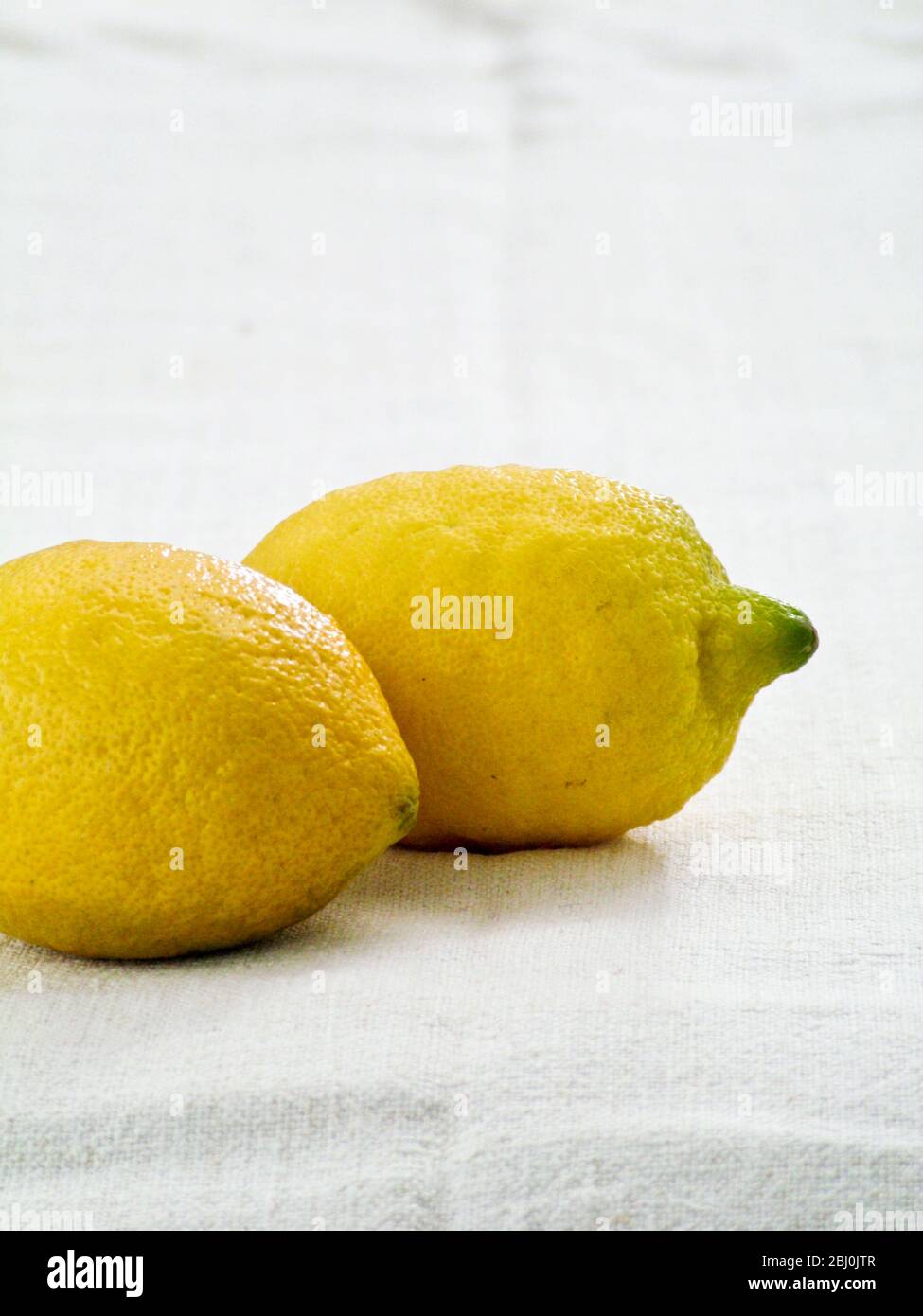 Two whole lemons on white linen cloth background - Stock Photo