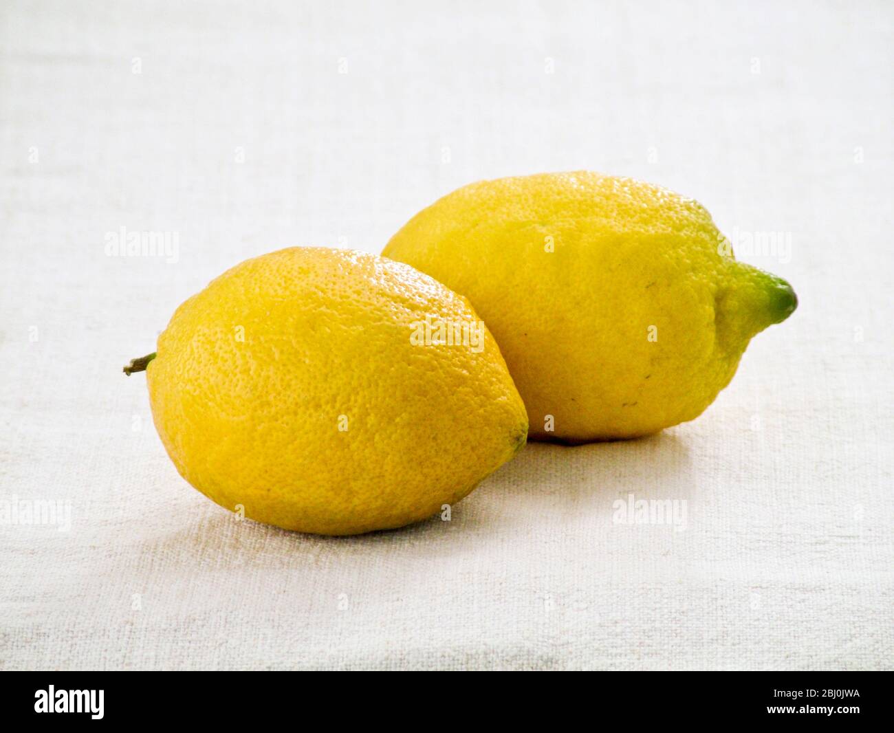 Two whole lemons on white linen cloth background - Stock Photo