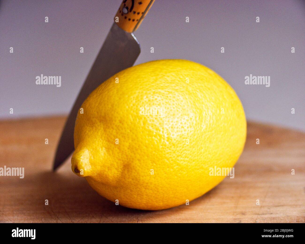 Whole fresh lemon with knife on cutting board - Stock Photo