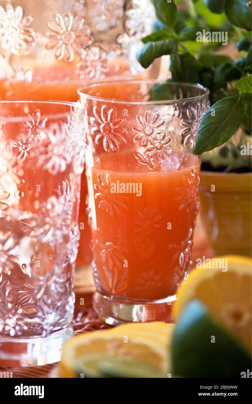 Pink grapefruit or mixed beakfast juice in decorative glass and jug with cut lemons and limes - Stock Photo