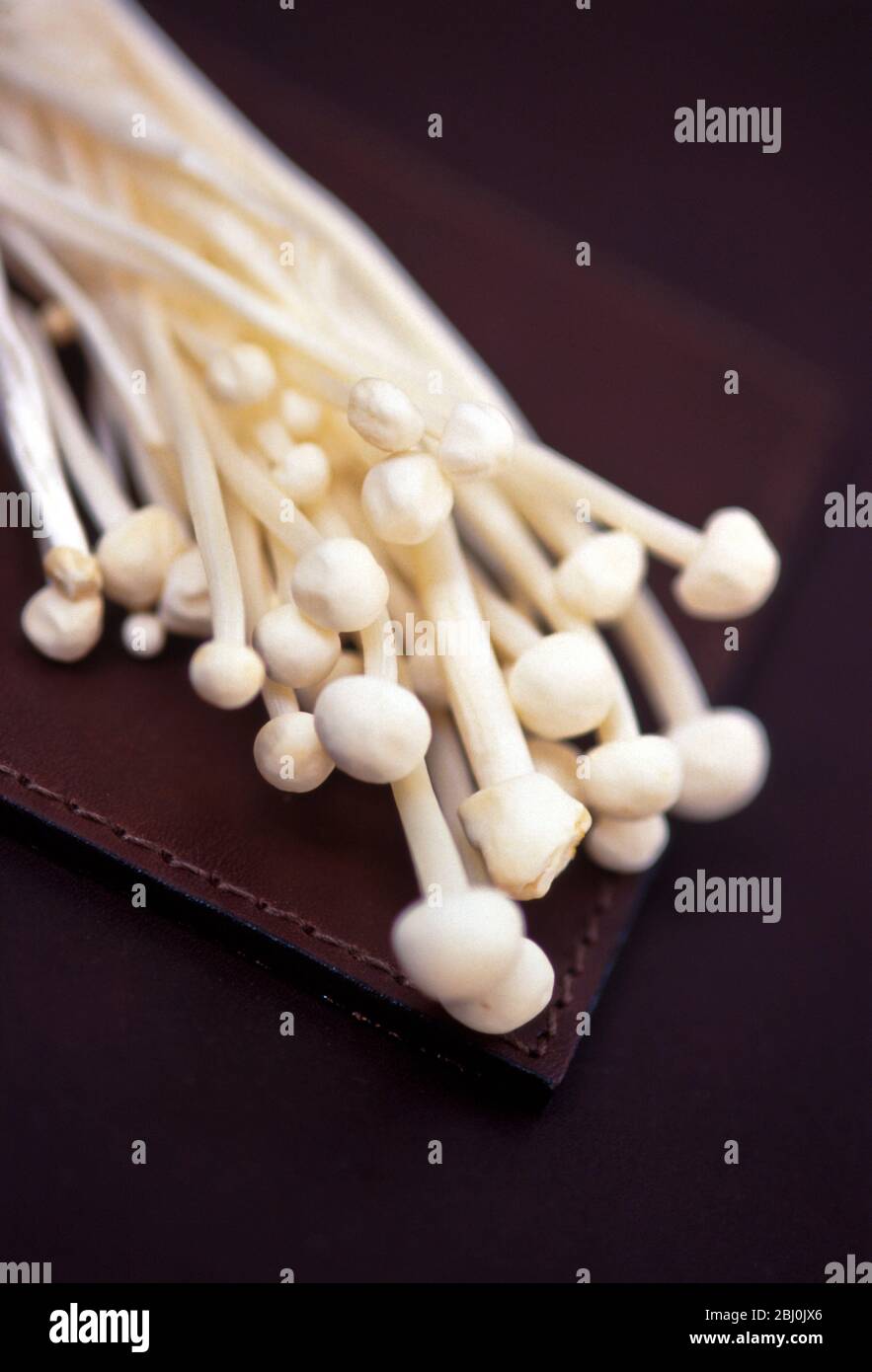 Detail of enoki mushrooms against brown background. Enotiake are long, thin white mushrooms used in Asian cuisines, particularly those of Japan, Korea Stock Photo