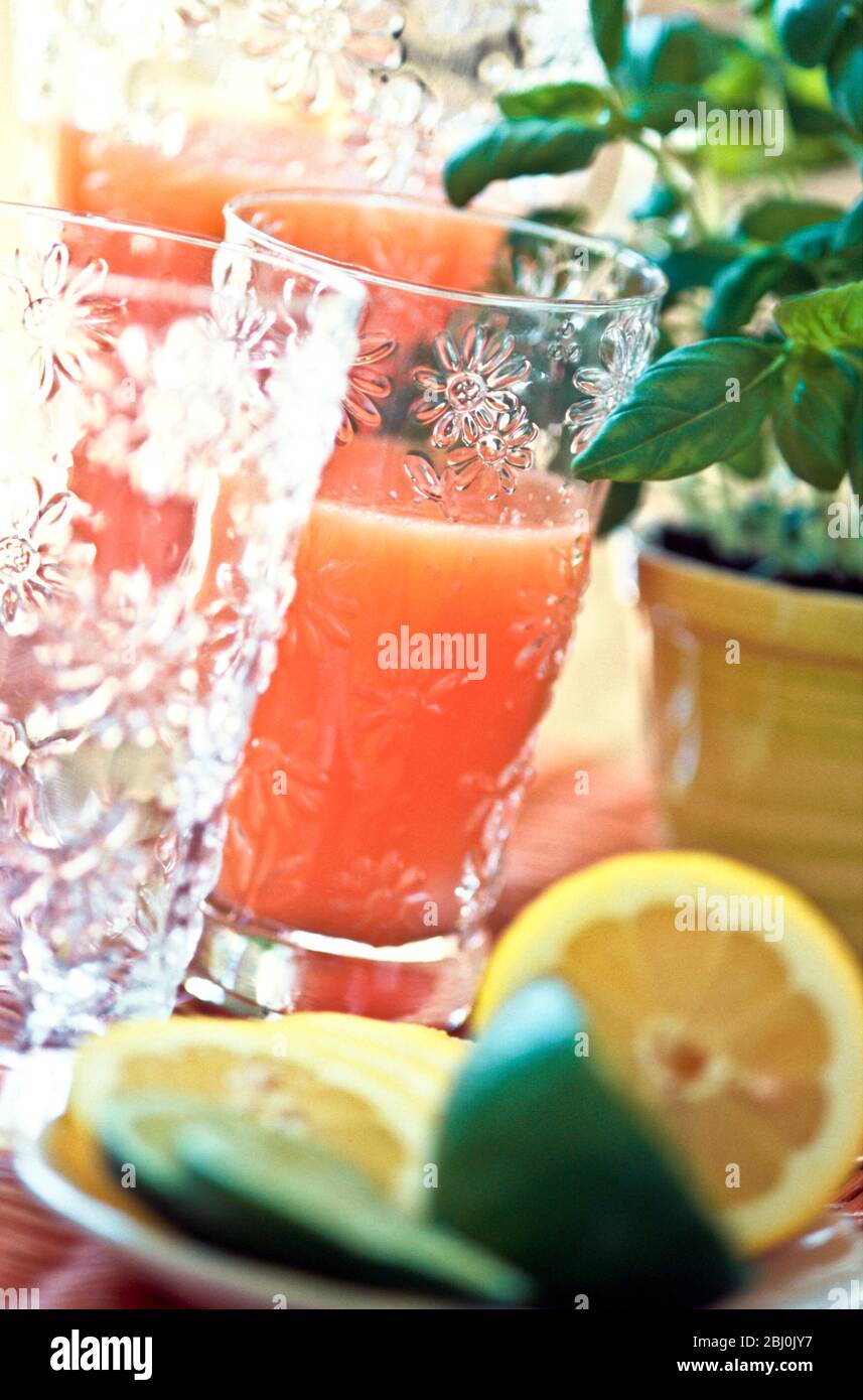 Pink grapefruit or mixed beakfast juice in decorative glass and jug with cut lemons and limes - Stock Photo