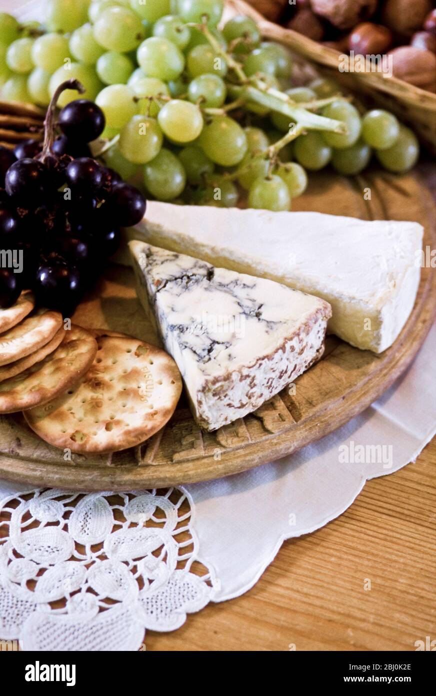 Cheeseboard of stilton and brie with water biscuits and white and black grapes - Stock Photo