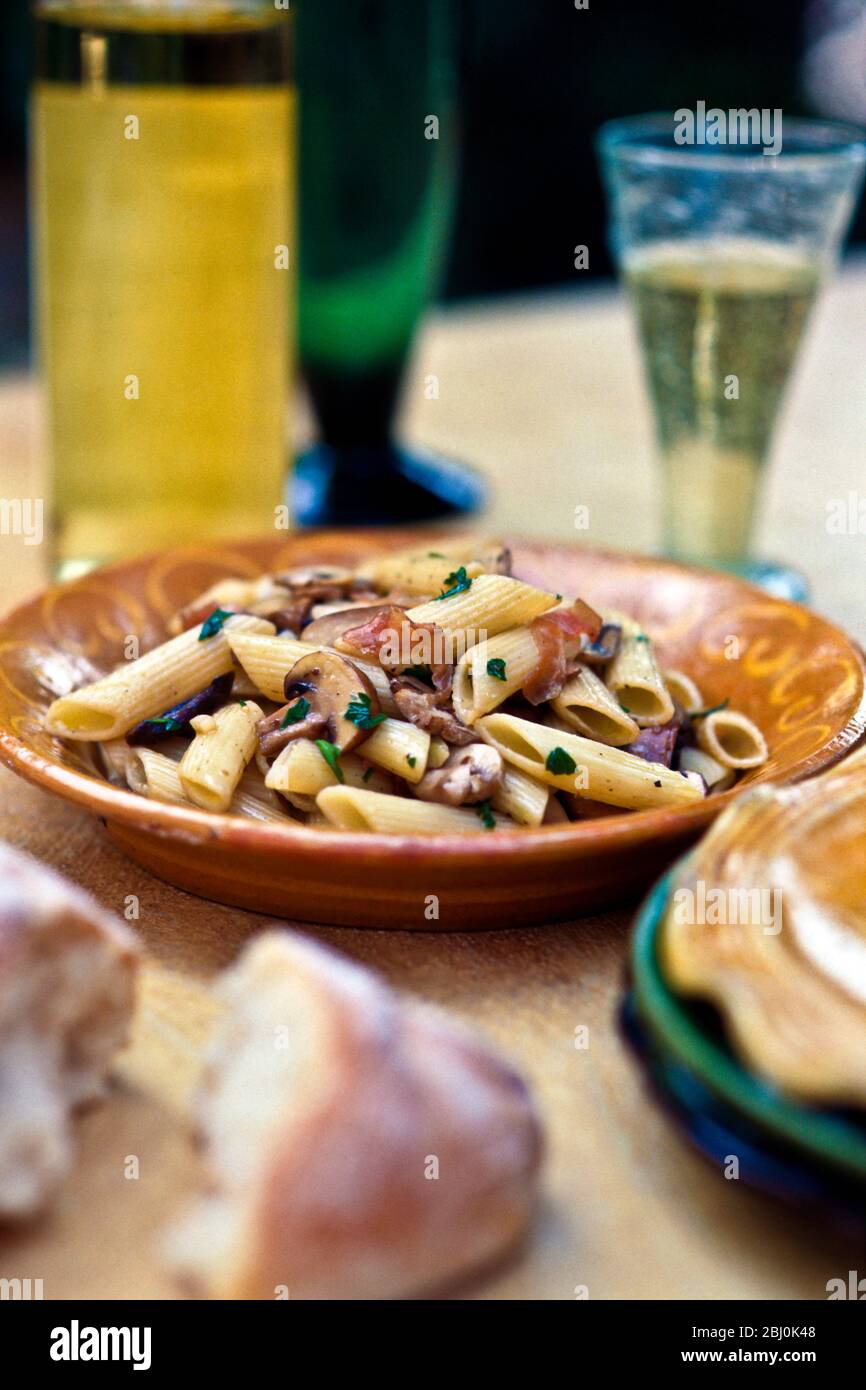 Penne pasta shpaes with mushrooms, parsley, prosciutto and olive oil - Stock Photo