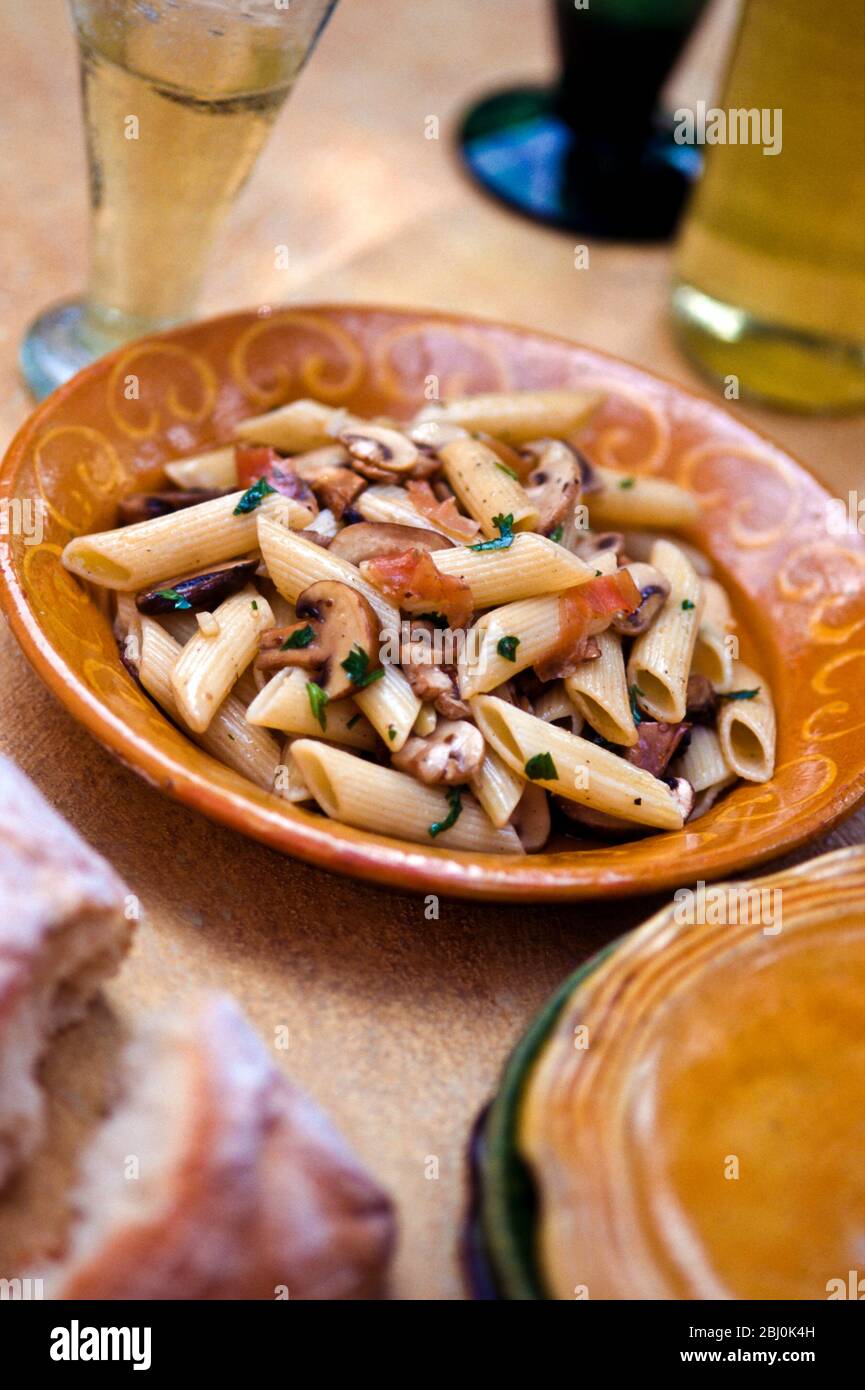 Penne pasta shpaes with mushrooms, parsley, prosciutto and olive oil - Stock Photo