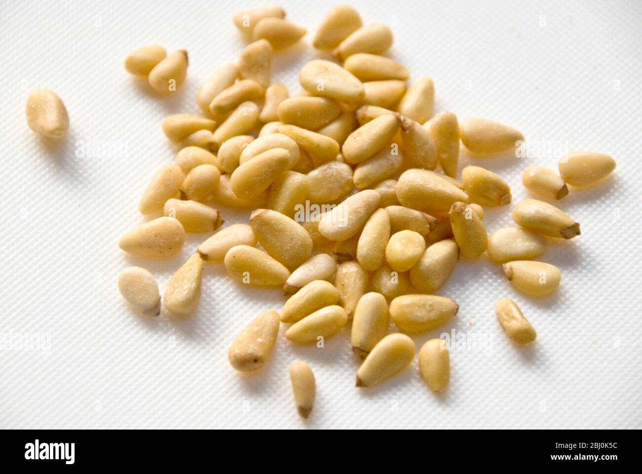Whole pinenuts in small heap on white surface - Stock Photo