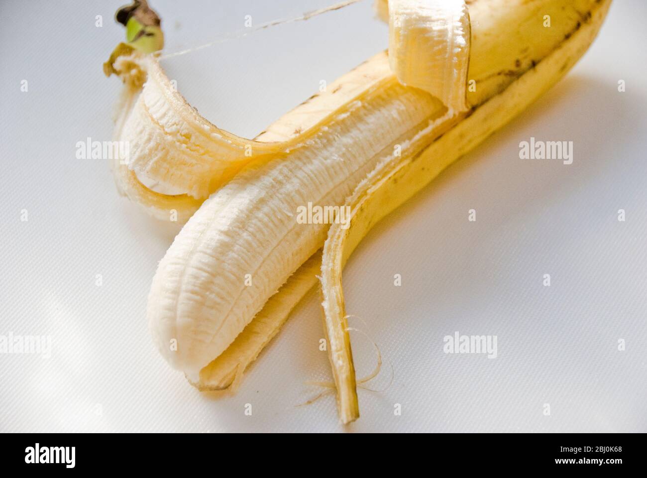Half peeled banana on white surface - Stock Photo