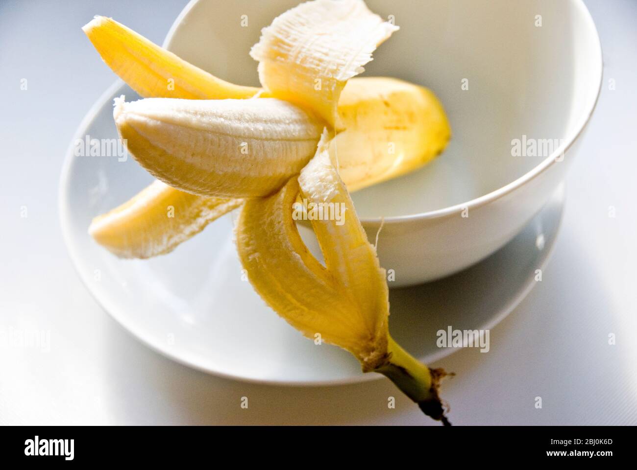 Half peeled banana in white bowl - Stock Photo