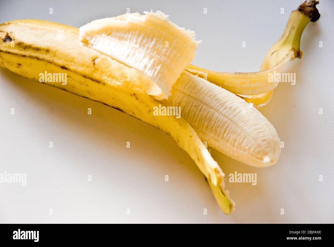 Half peeled banana on white surface - Stock Photo