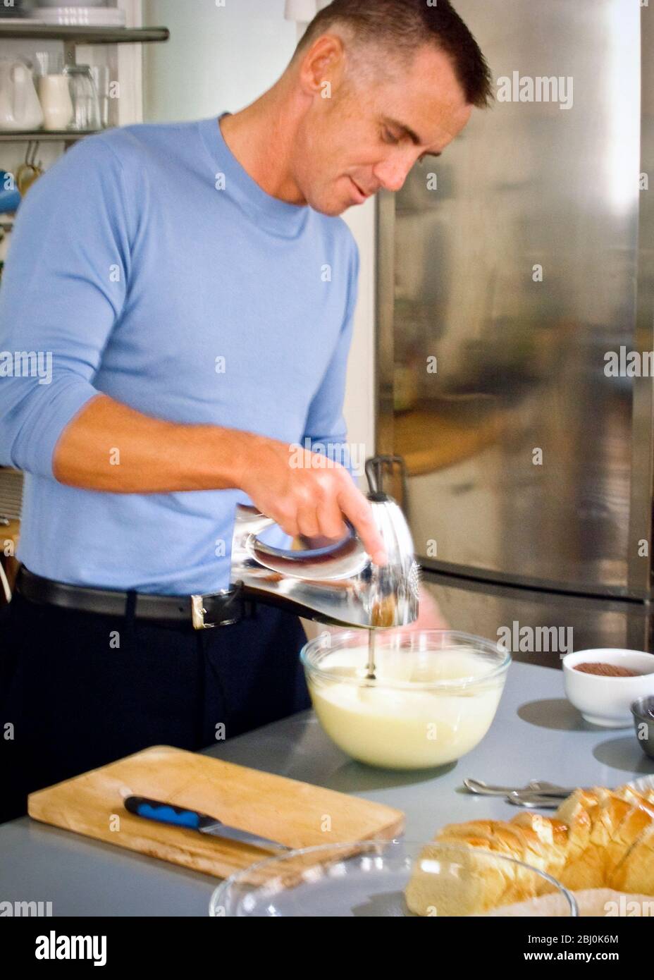 Gary Rhodes in domestic kitchen whisking ingredients for an orange dessert - Stock Photo