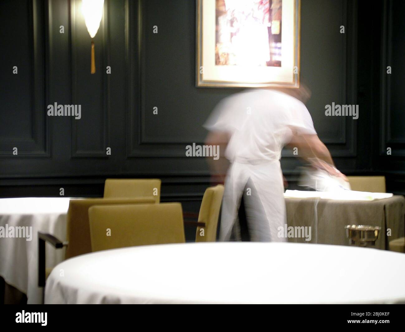 Pressing white linen table cloth in dark restaurant interior before service - Stock Photo