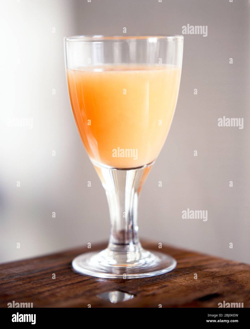 Grapefruit juice in stemmed glass on corner of table - Stock Photo