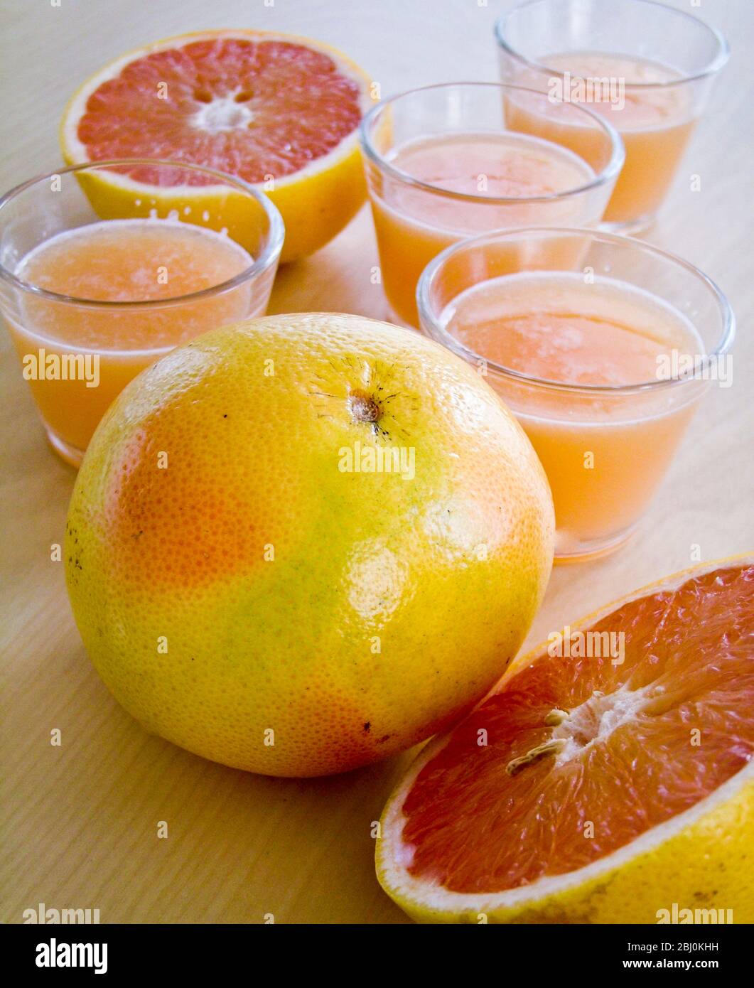 Little glasses of pink grapefruit juice with whole and halved grapefruit - Stock Photo