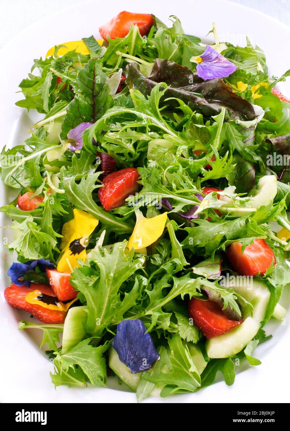 Pretty salad with mixed baby leaves, rocket, cucumber, strawberries and pansy flowers - Stock Photo