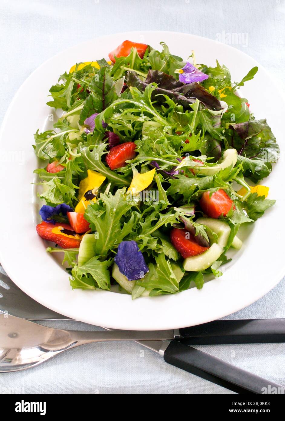 Pretty salad with mixed baby leaves, rocket, cucumber, strawberries and pansy flowers - Stock Photo