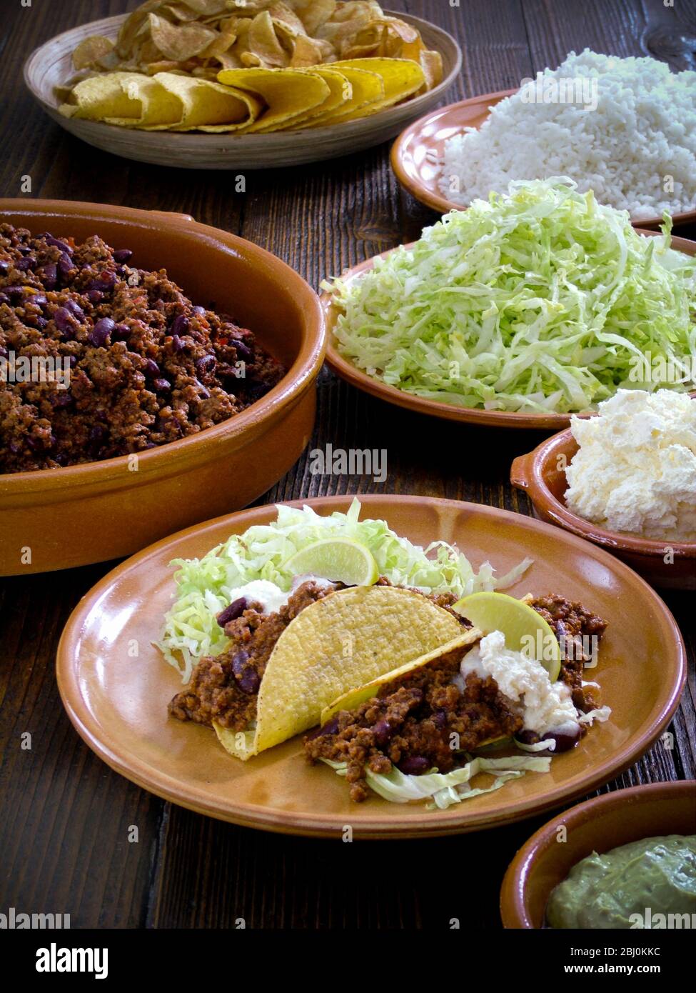 Mexican meal of tacos with chilli con carne shredded lettuce, plain rice, and sour cream - Stock Photo