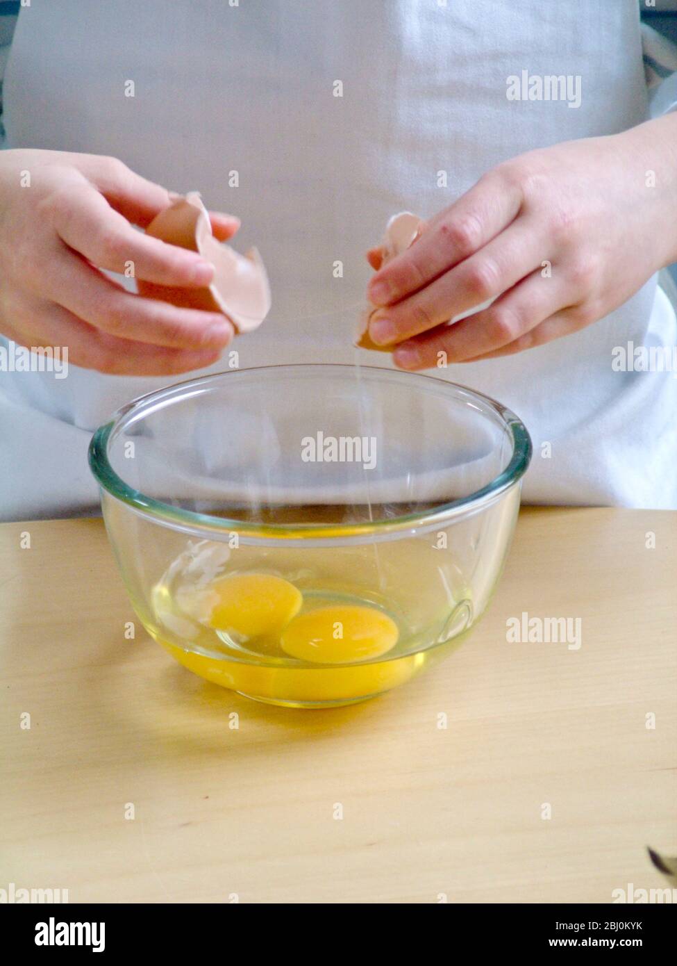 Child breaking eggs into glass bowl, learning how to make scrambled eggs. - Stock Photo