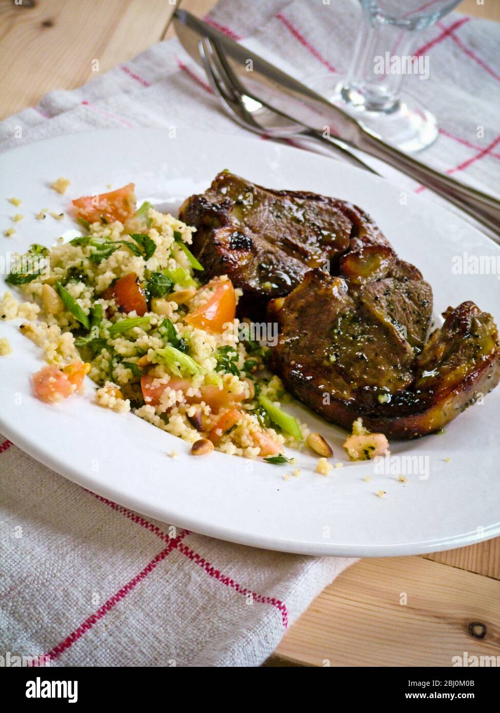 Two lamb chops with couscous with vegetables on white plate - Stock Photo