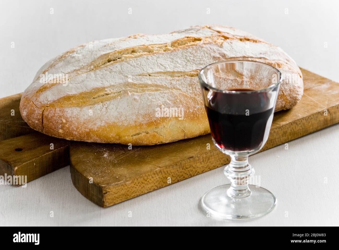 Glass of red wine with crusty rustic white loaf on wooden board - Stock Photo