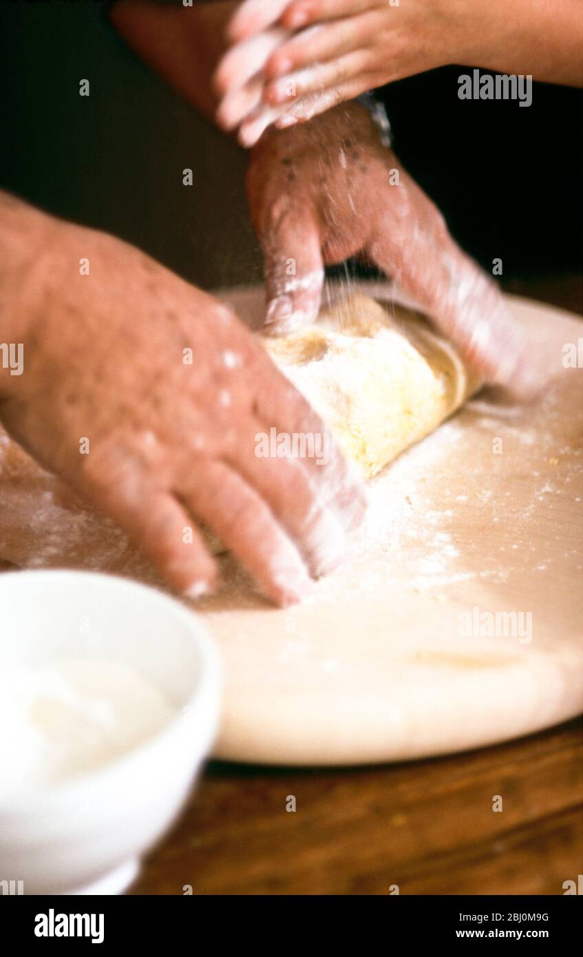 Chef kneading and rolling pastry with little girl helping - hands only shown - Stock Photo