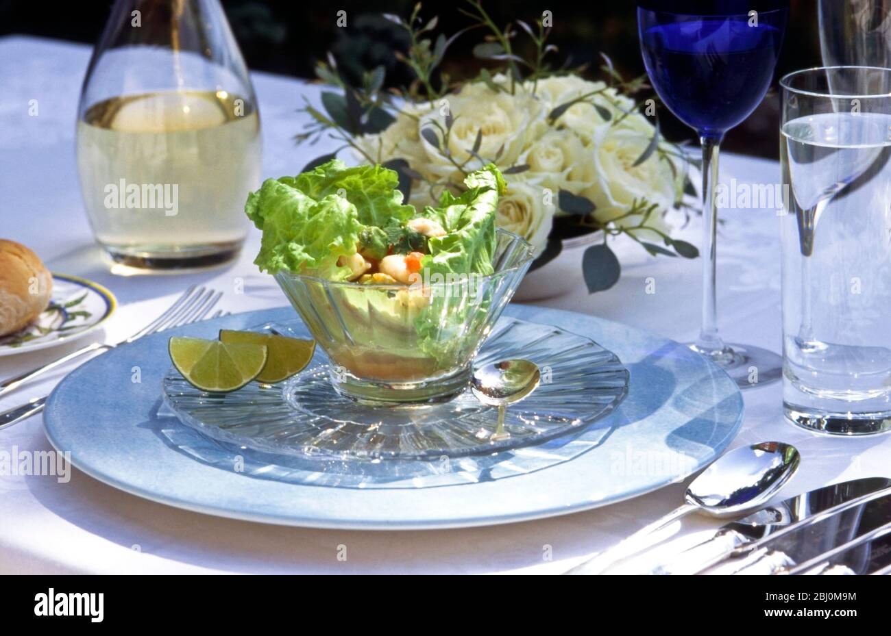 Seafood salad in crystal glass bowl in formal table setting outdoors - Stock Photo