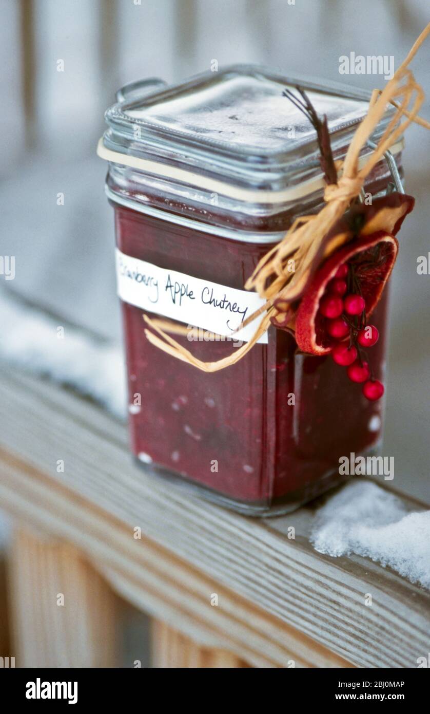 Cranberry apple chutney in decorated jar sitting outside on deck railing in snow - Stock Photo