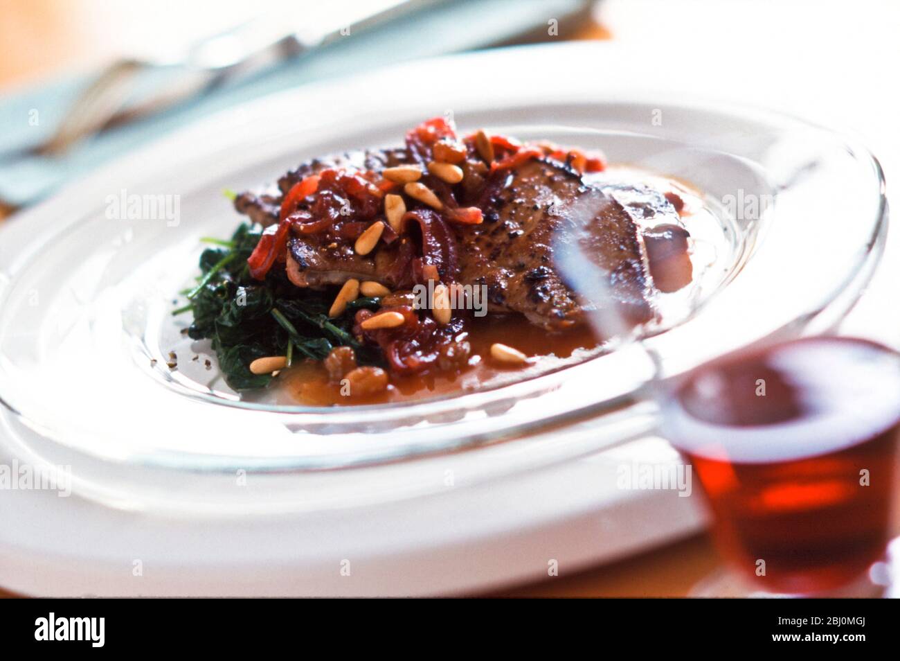 Calves liver with sauce of red onions, wine and pine nuts on bed of spinach. - Stock Photo