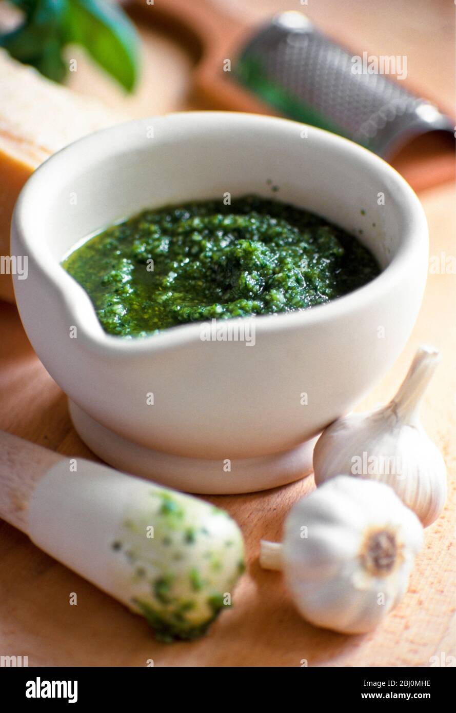 Making home made pesto in pestle and mortar with ingredients around - Stock Photo