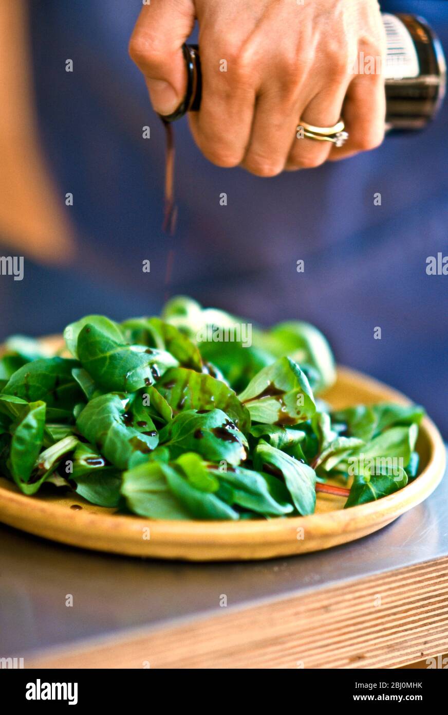 Drizzling balsamic vinegar onto lamb's lettuce in pottery dish. - Stock Photo