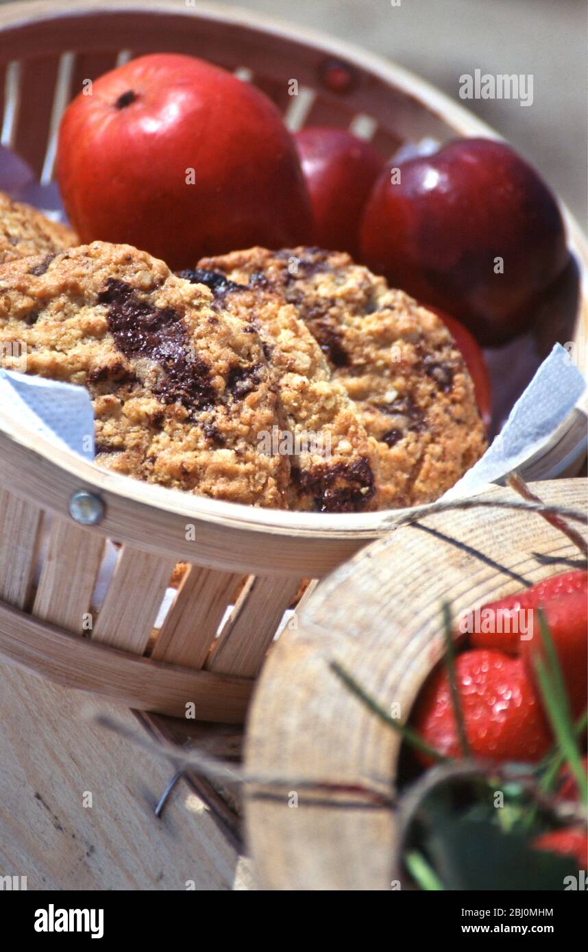 Choc chip cookies and shiny red apples in basket as part of beach picnic - Stock Photo