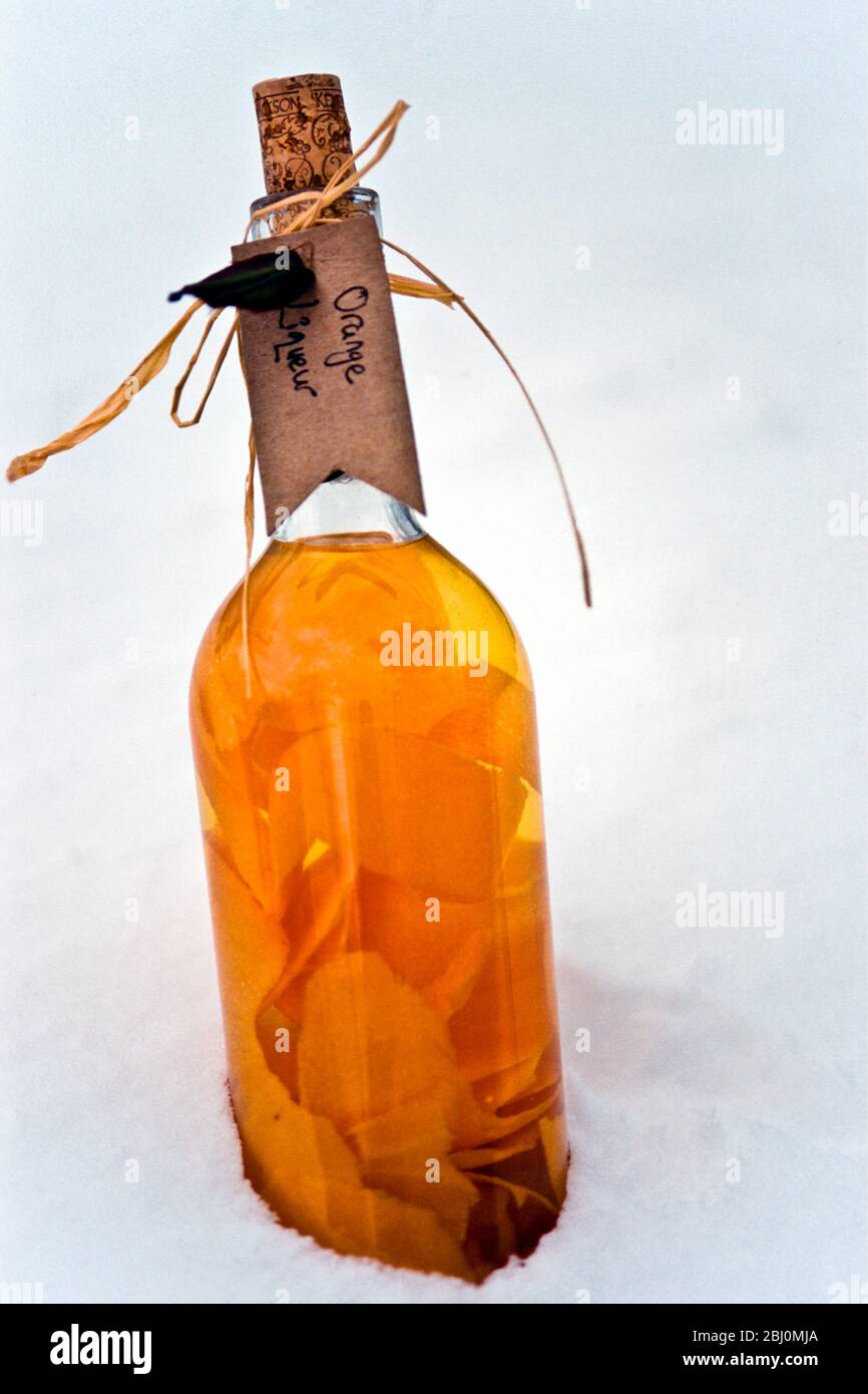 Homemade gift bottle of orange liqueur being chilled in snow outdoors - Stock Photo