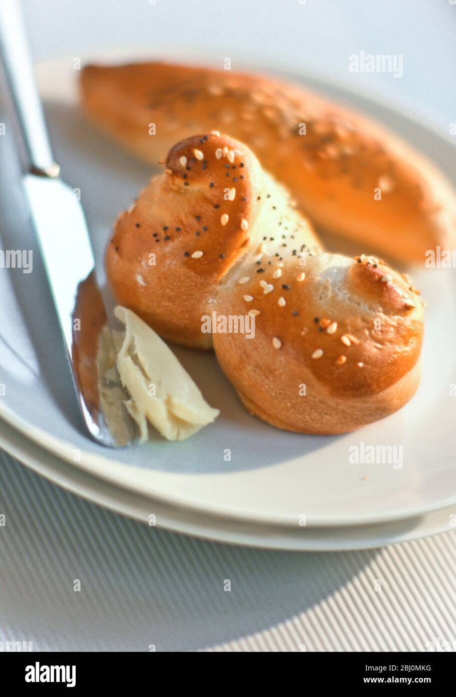 Sesame seeded white bread rolls with butter - Stock Photo