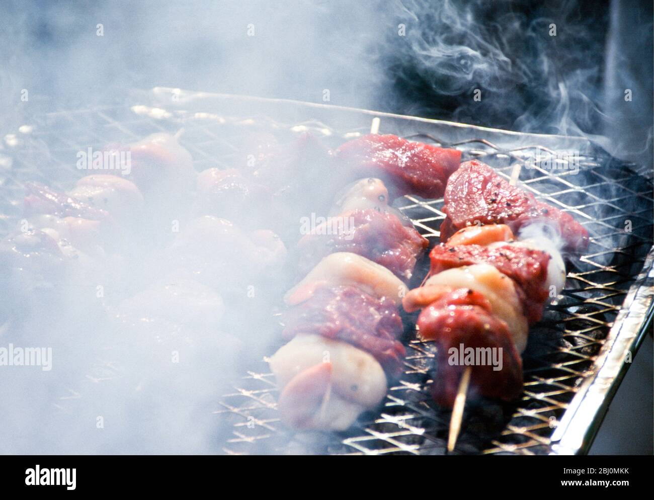 Grilling scallop and steak kebabs on a charcoal fired barbecue grill - Stock Photo