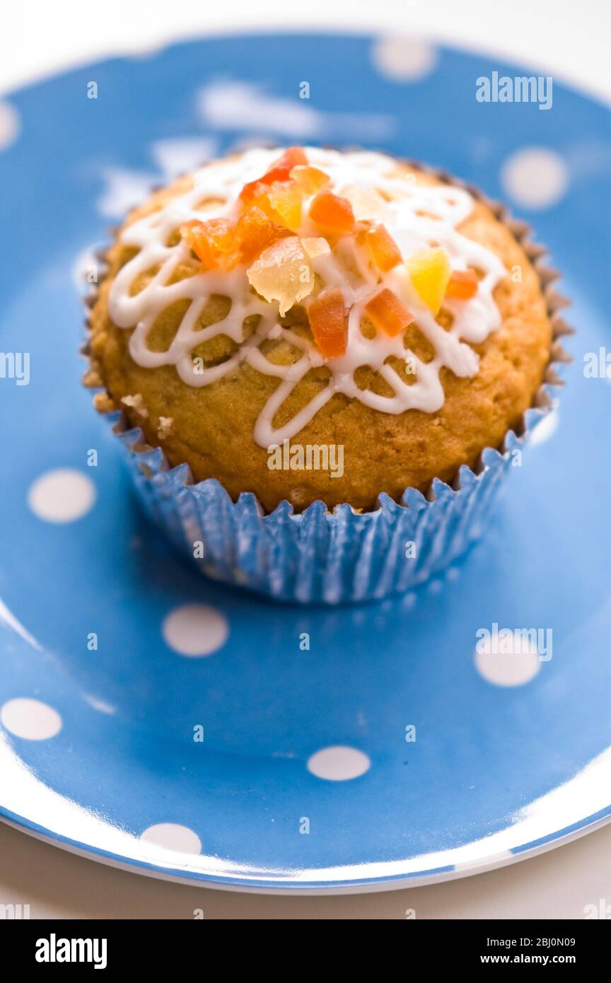 Muffin decorated with squiggly icing and candied peel on spotted blue plate - Stock Photo