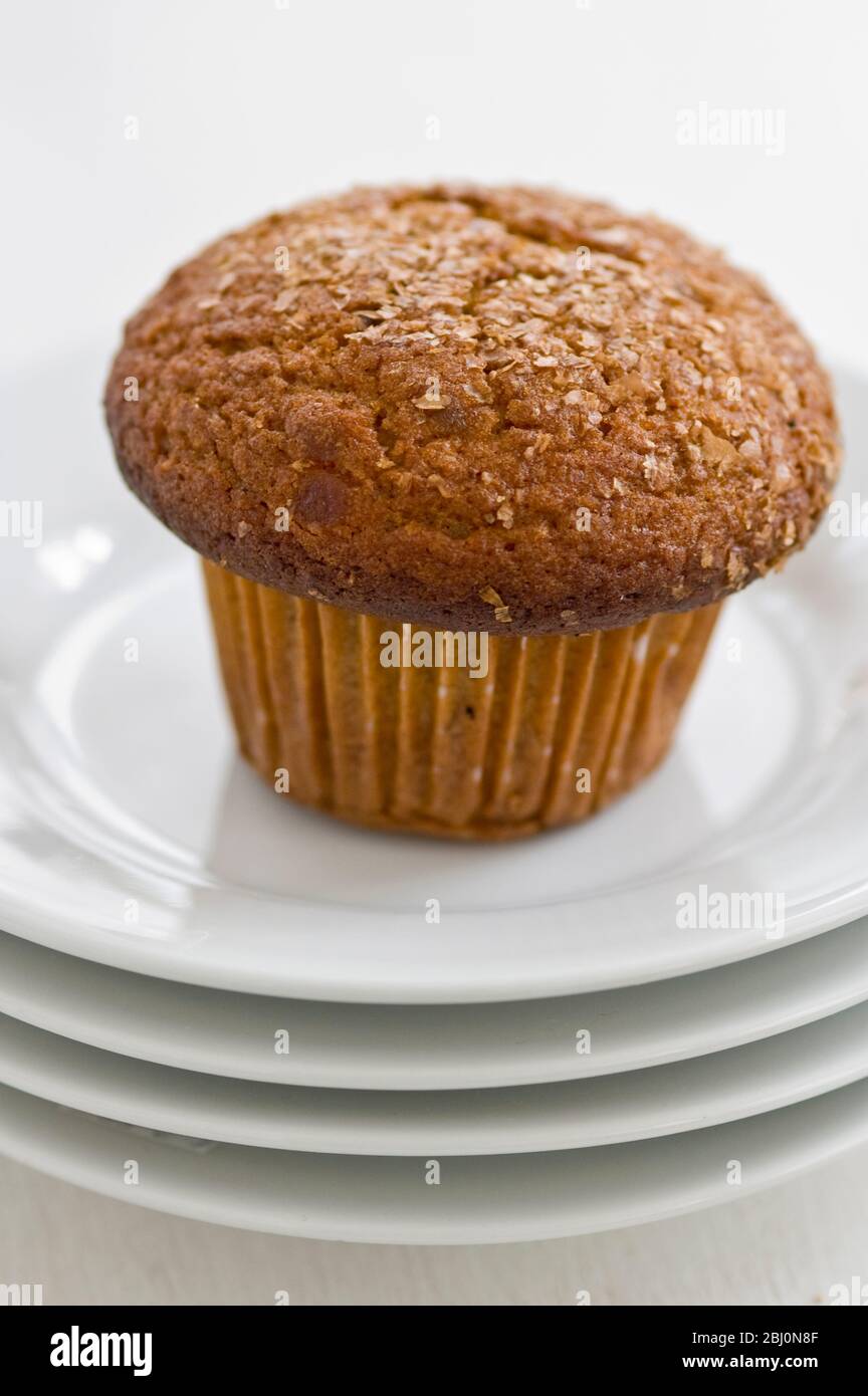 Cinnamon bran muffin on stack of white plates with cup of black coffee - Stock Photo