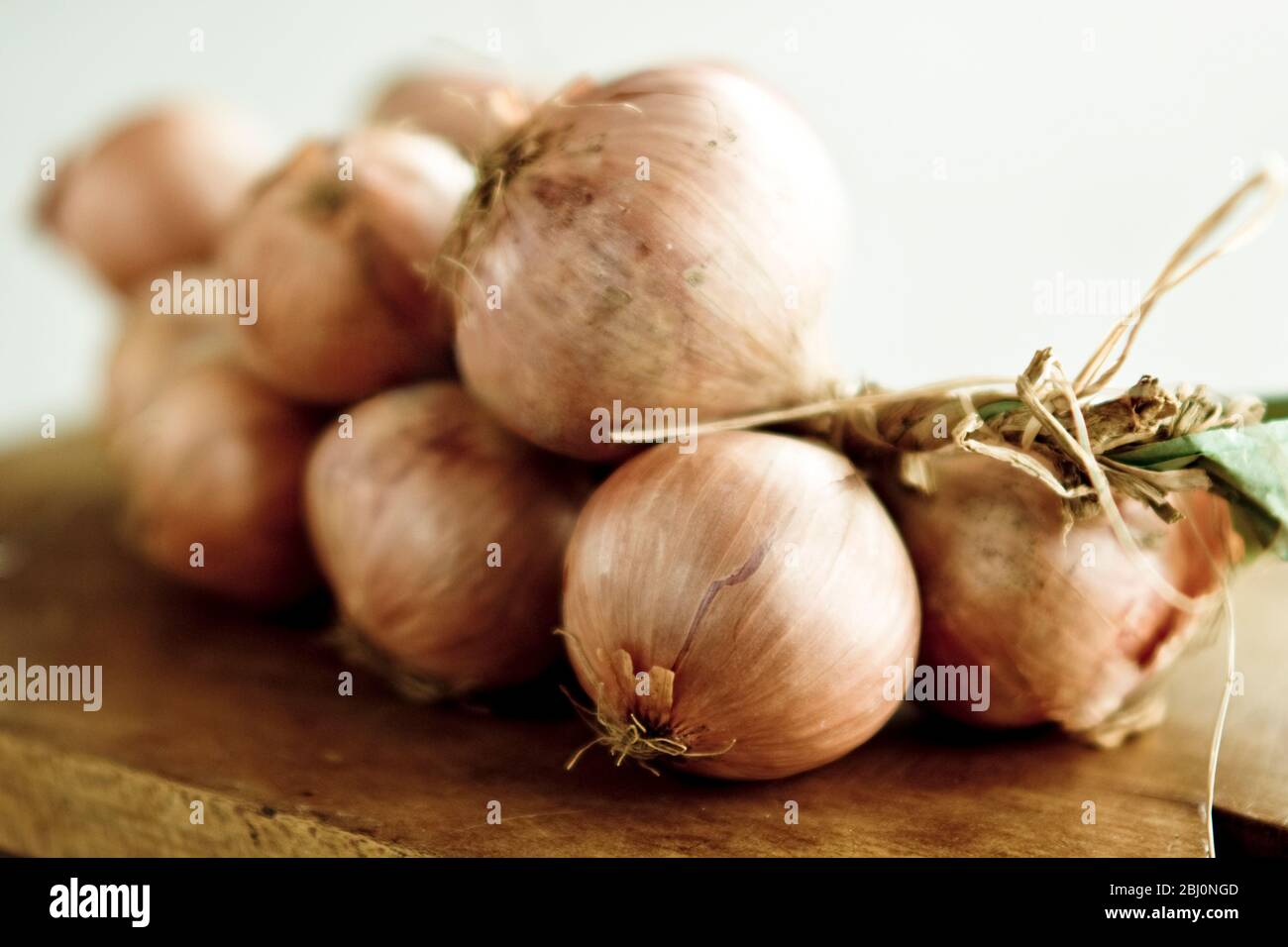 String of onions lying on wooden board - Stock Photo