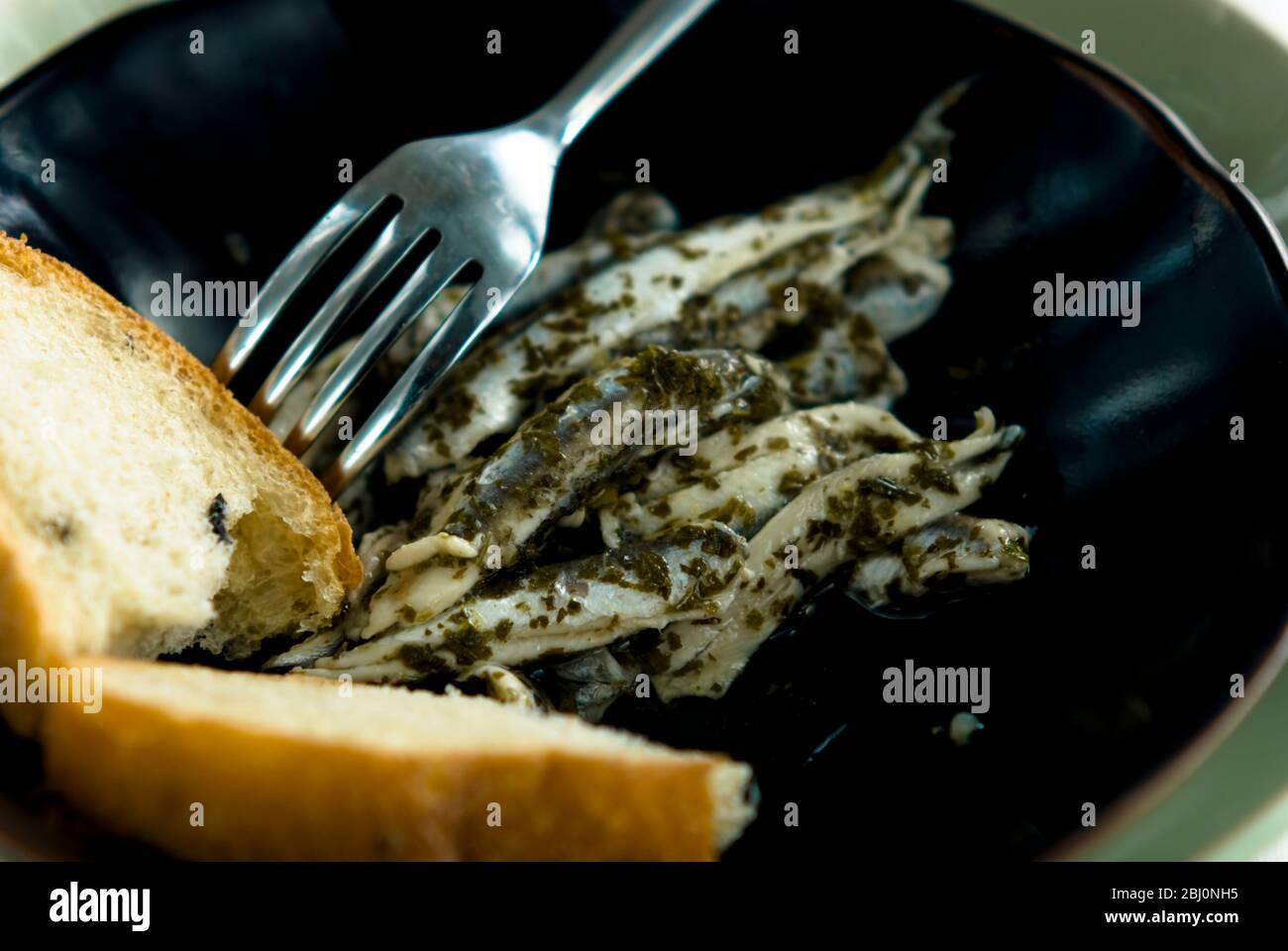 Marinated Italian anchovies with bread on black pottery plate - Stock Photo