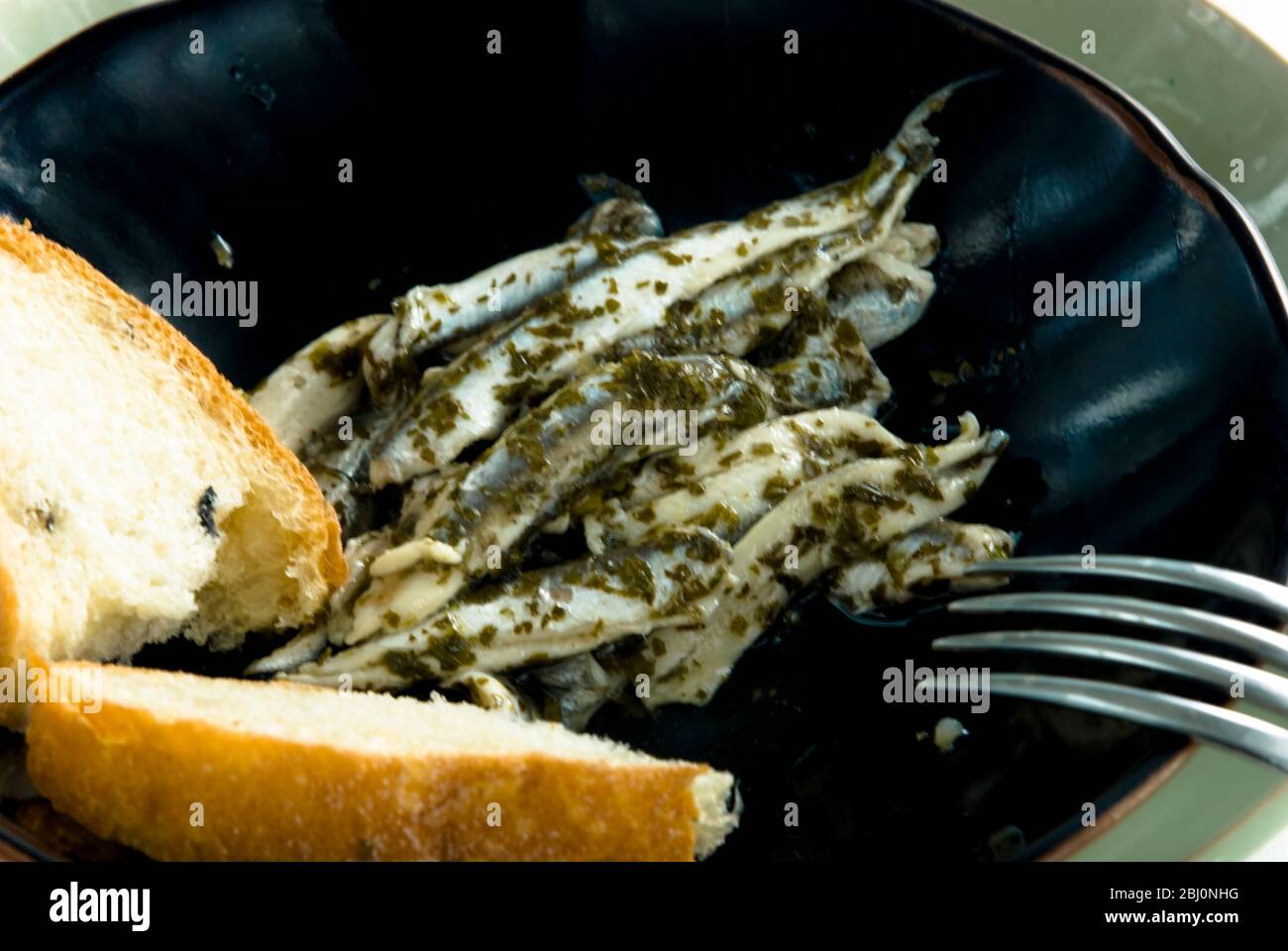 Marinated Italian anchovies with bread on black pottery plate - Stock Photo