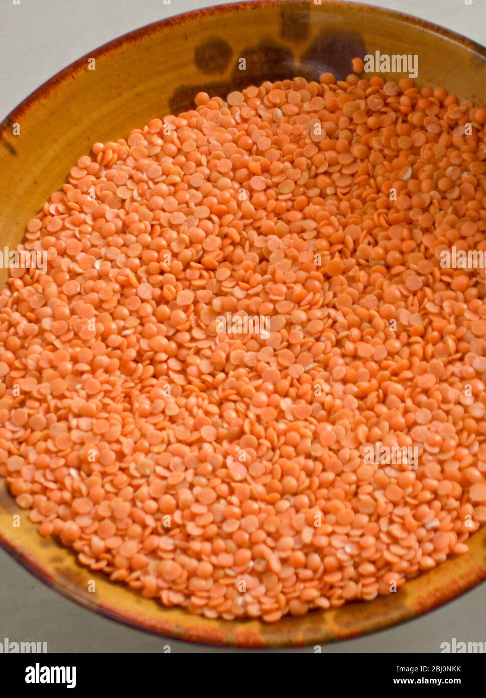 Pottery bowl of raw red split lentils - Stock Photo