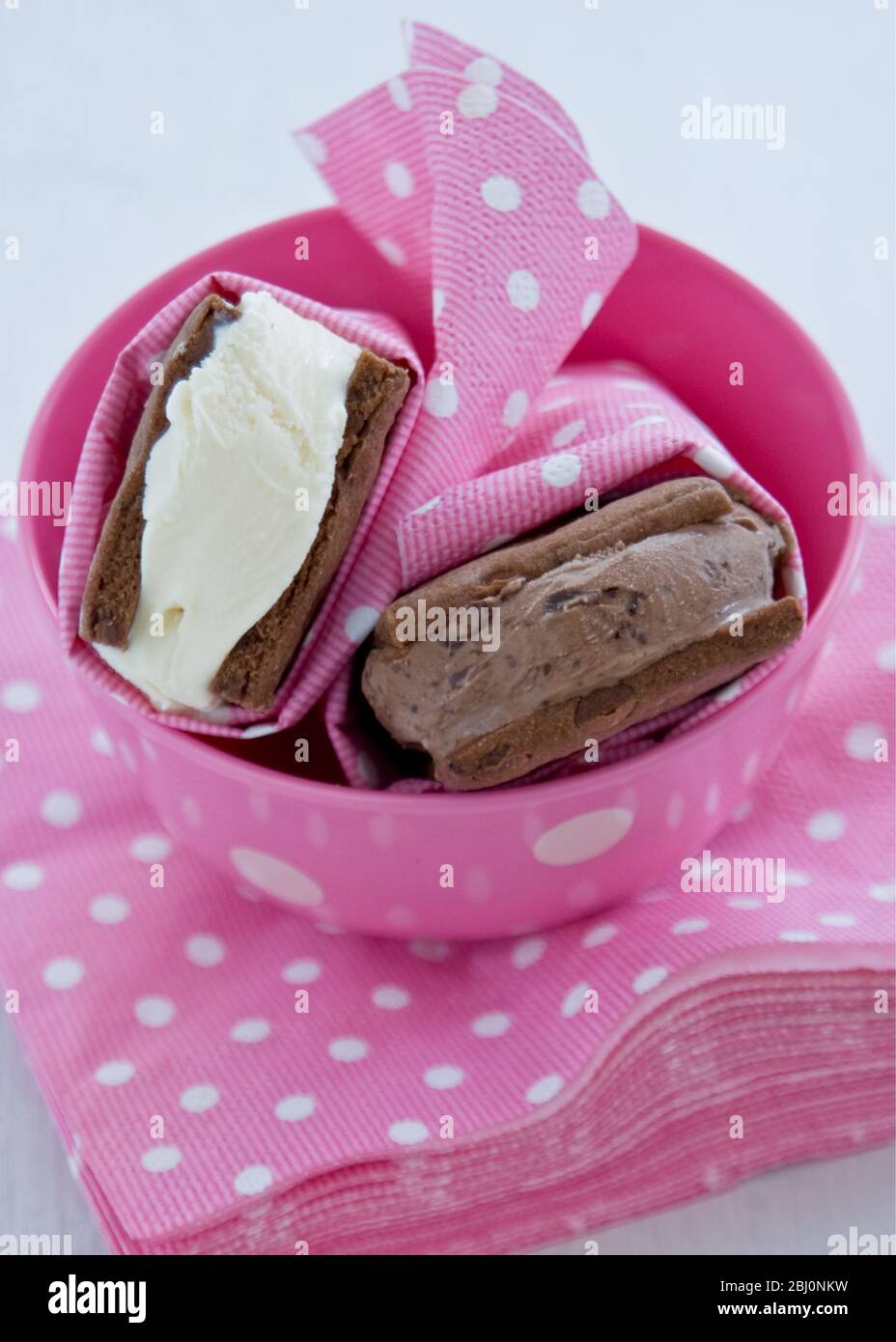 Chocolate and vanilla icecream in homemade chocolate biscuits wrapped in spotty pink and white paper napkins, in matching bowl - Stock Photo