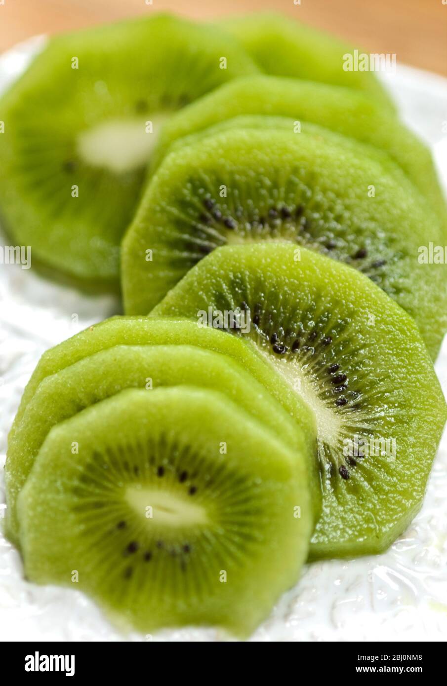 Slices of peeled kiwi fruit on white textured plate - Stock Photo