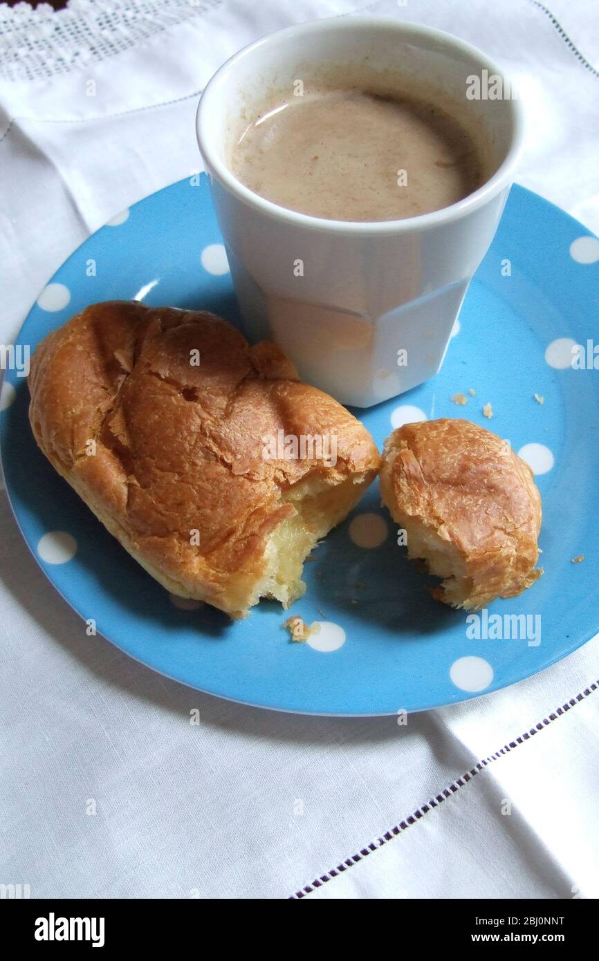 White mug of coffee in blue spotted plate with croissant on white linen cloth with lace edging. Vintage style - Stock Photo
