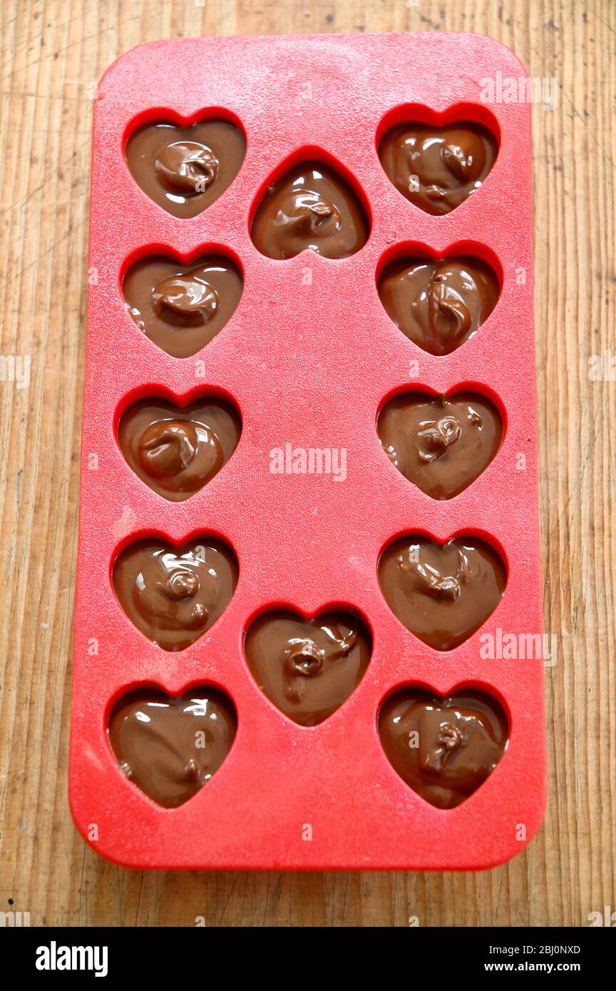 Making heart shaped in chocolates for Valentine's day in red heart shaped mould - Stock Photo