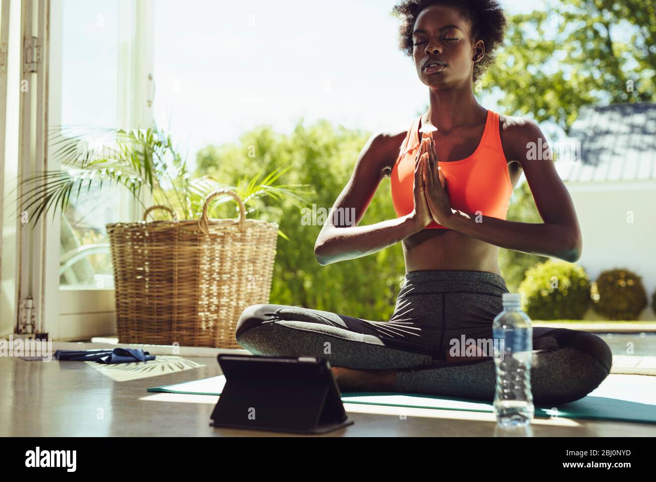 Healthy woman sitting on yoga meditation at home with a digital tablet in front. Fitness woman in sportswear meditating in lotus yoga pose indoors. Stock Photo