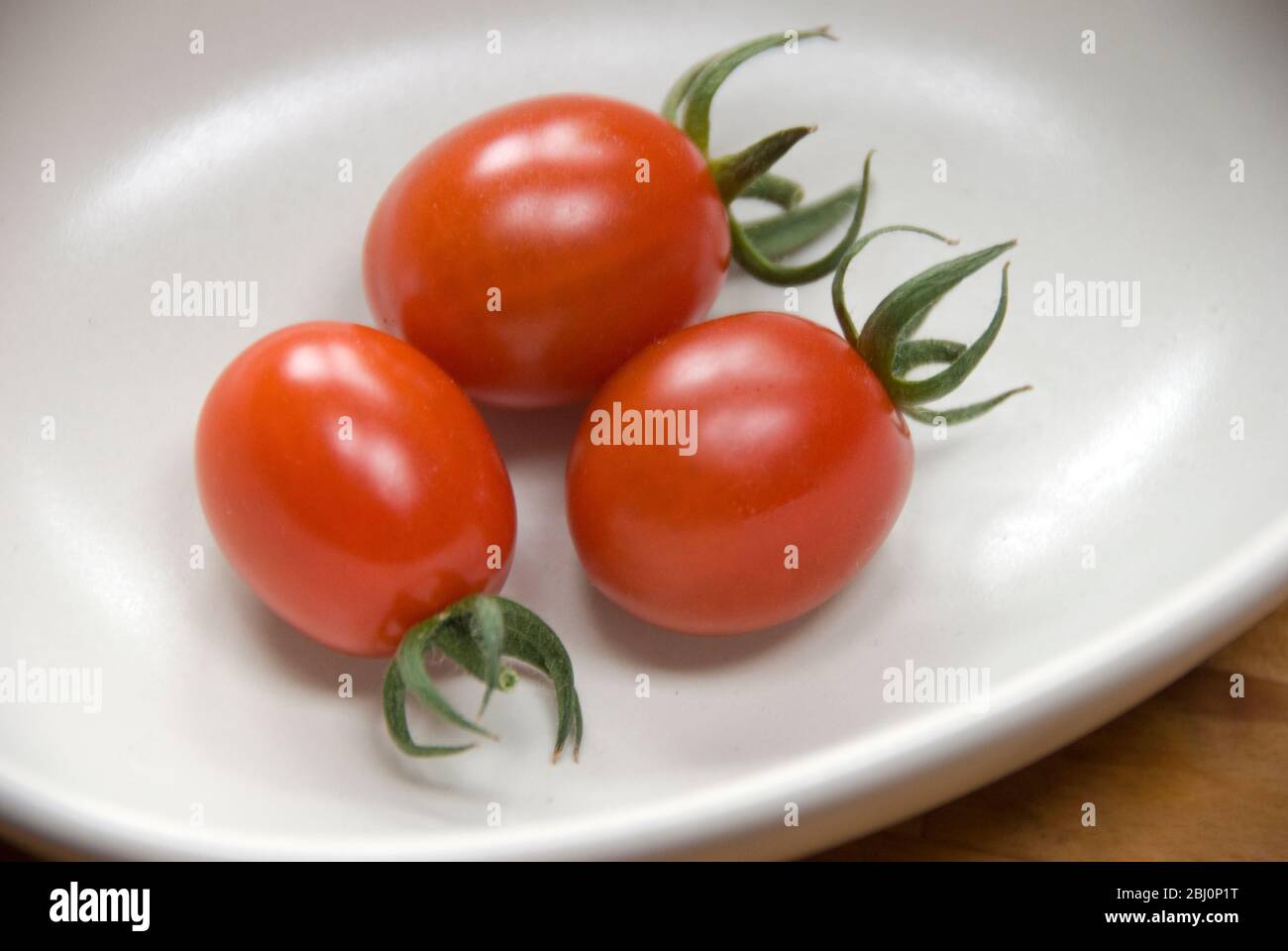 Three home grown plum tonatoes in small dish - Stock Photo