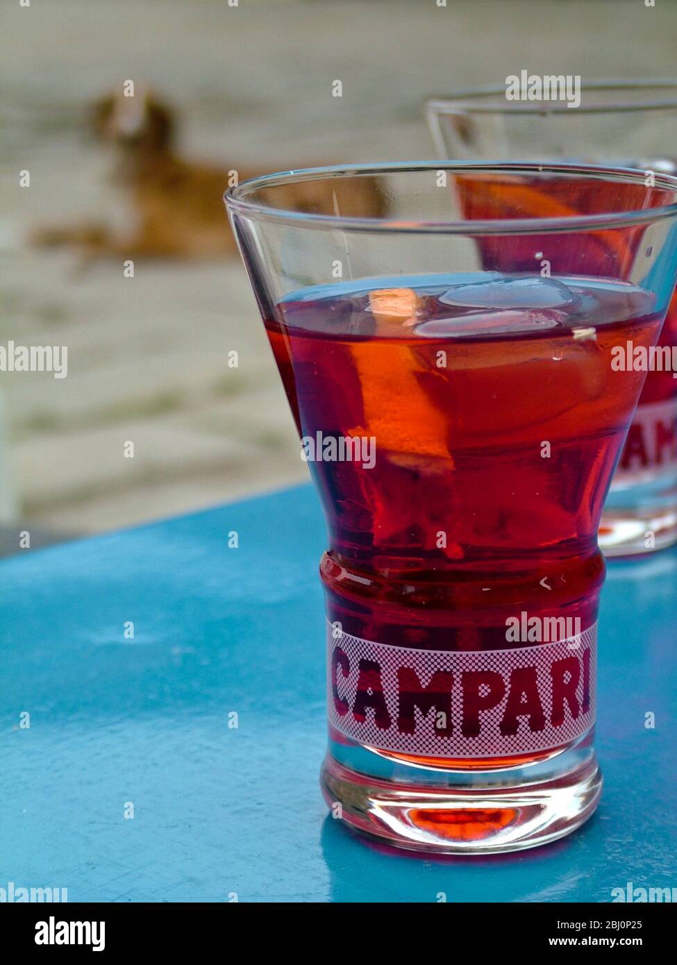 Campari glass of campari on table of outdoor cafe in Italy - very near French border - with dog in the background. - Stock Photo